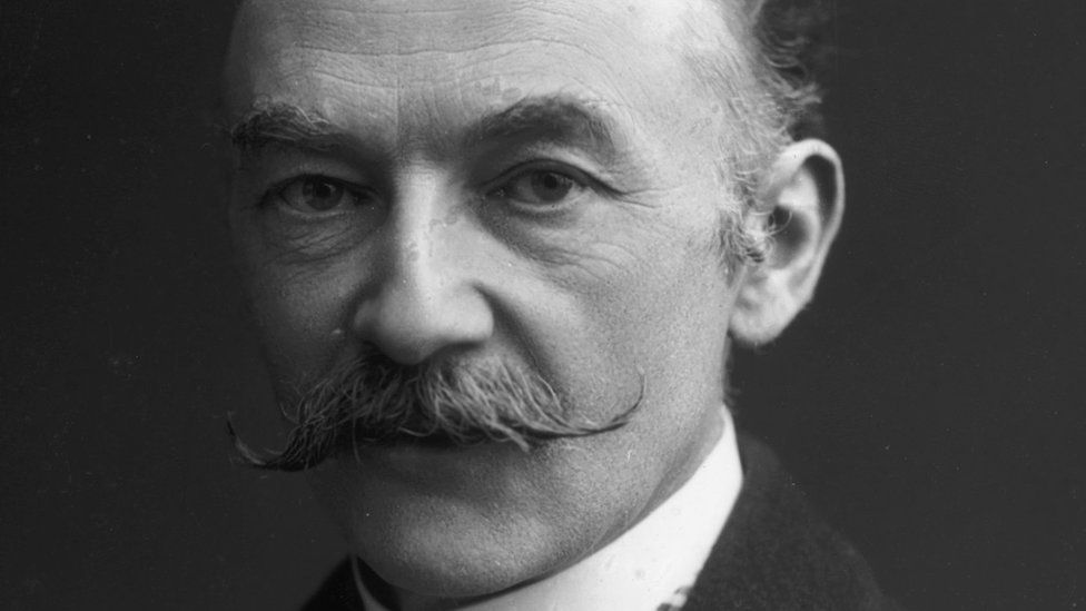 A black and white photograph of the English writer Thomas Hardy as a man in his late 40s or early 50s, sporting a handlebar moustache.